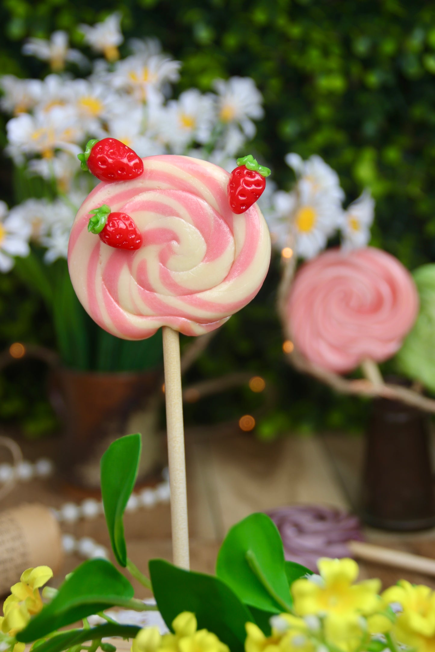 Sucette foraine artisanale en spirale, parfumée à la vanille et à la fraise, décorée de petites fraises sculptées à la main. Une gourmandise élégante et fruitée, parfaite pour le printemps.