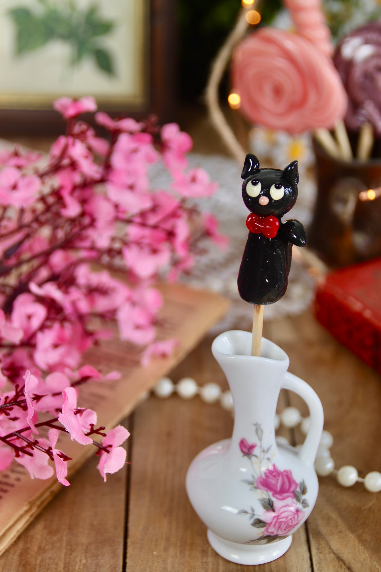 Sucette chat cassis posée dans un décor féerique aux couleurs rouges et violettes, accompagnée d’éléments de conte enchanté.
