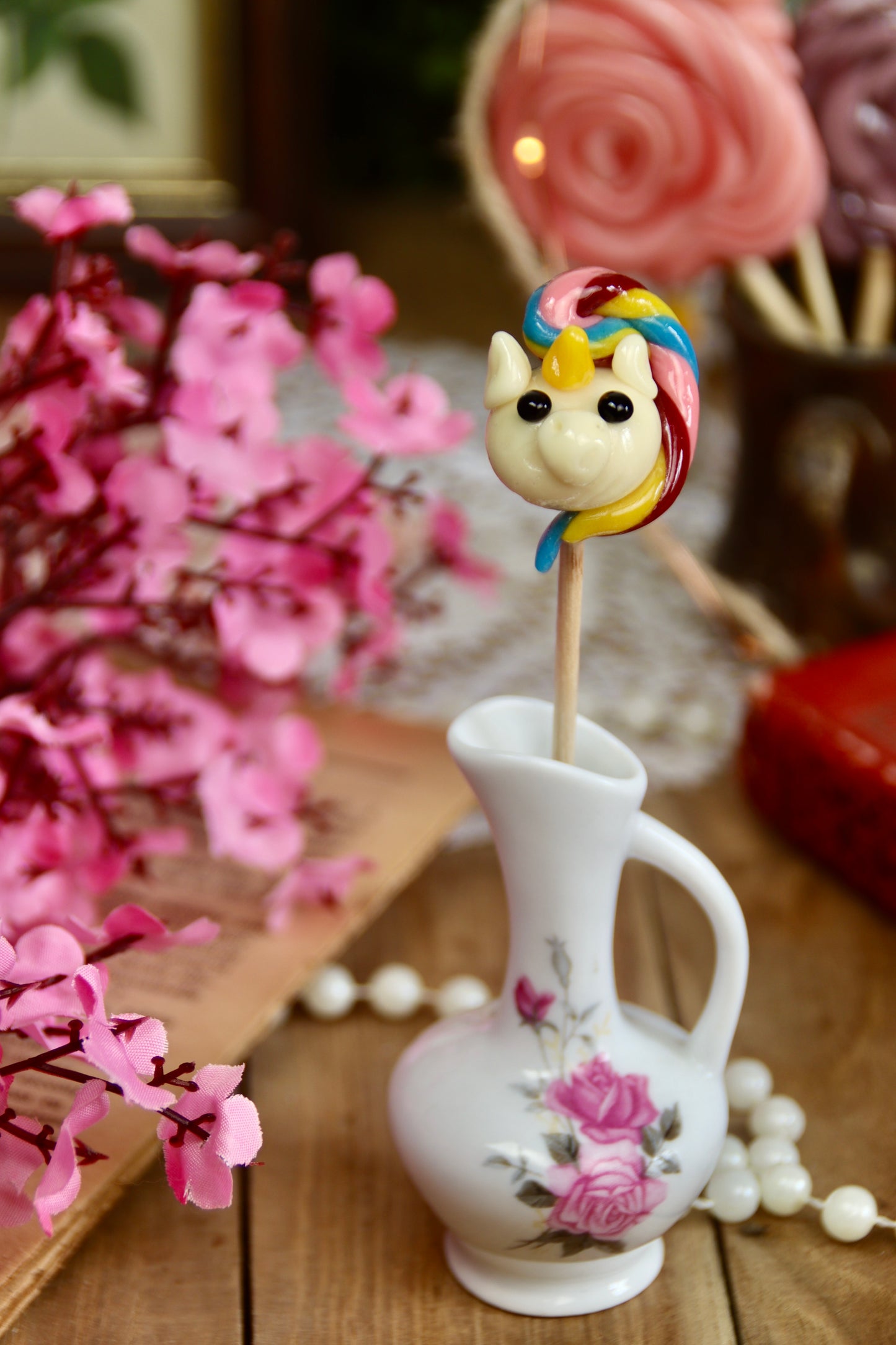 Sucette licorne dans une mise en scène féerique avec accessoires pastel, confiserie artisanale idéale pour cadeau enfant, décoration de table ou anniversaire magique.