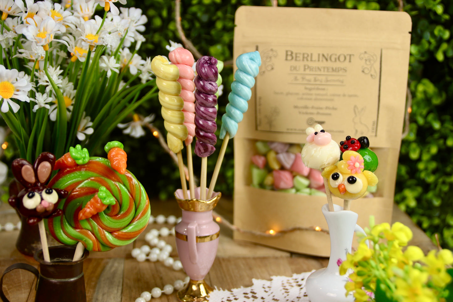 Photo du lot spĂ©cial printemps composĂ© de sucettes artisanales : cinq torsades aux couleurs pastel (myrtille, fraise, pĂȘche, violette et pomme), quatre sucettes sculptĂ©es reprĂ©sentant un poussin, une coccinelle, un lapin et un mouton, un sachet de 100g de berlingots colorĂ©s, et une grande sucette foraine pomme-orange dĂ©corĂ©e de petites carottes.