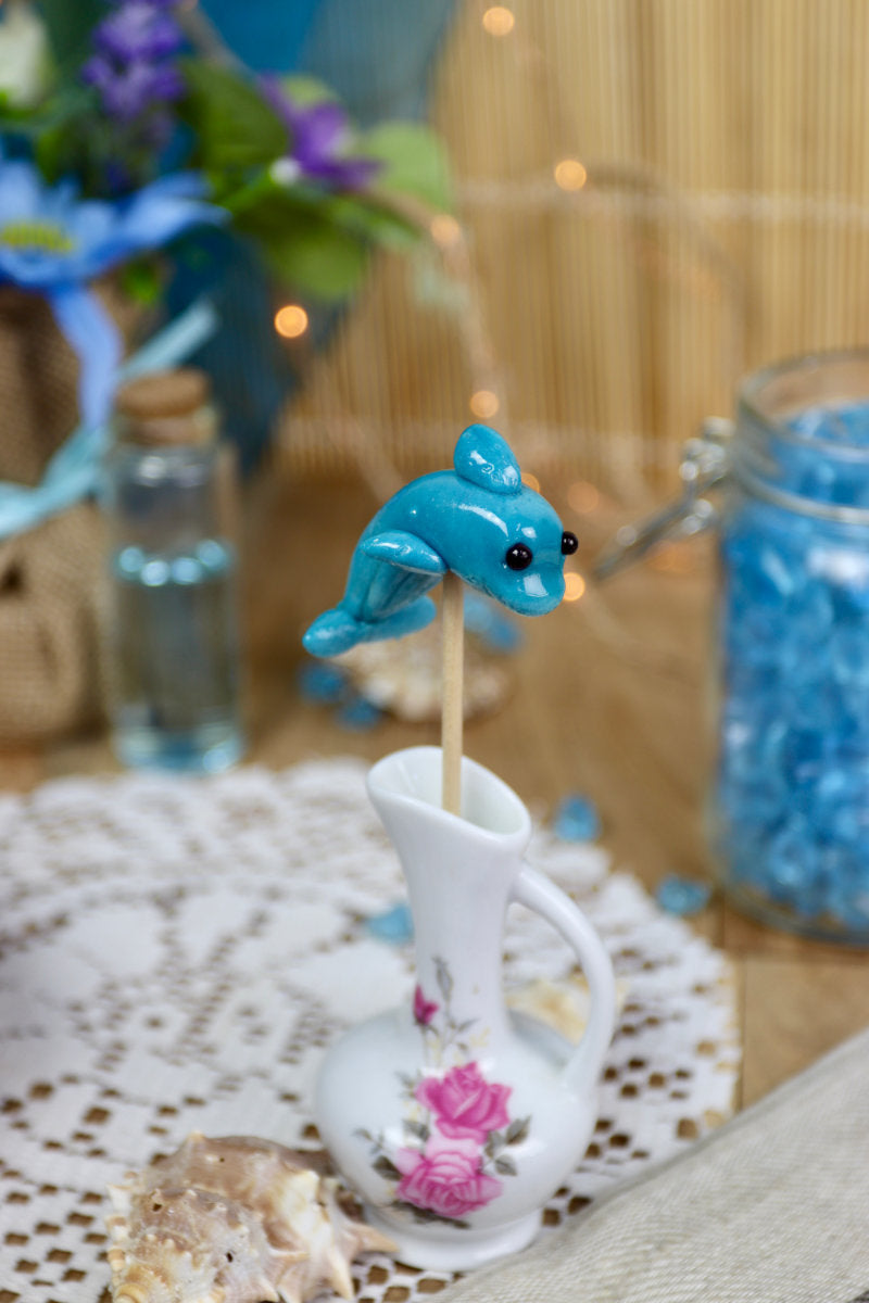 Sucette dauphin à la myrtille dans un décor marin, entourée de coquillages et d’éléments océaniques, parfaite pour un thème océan ou une décoration gourmande.