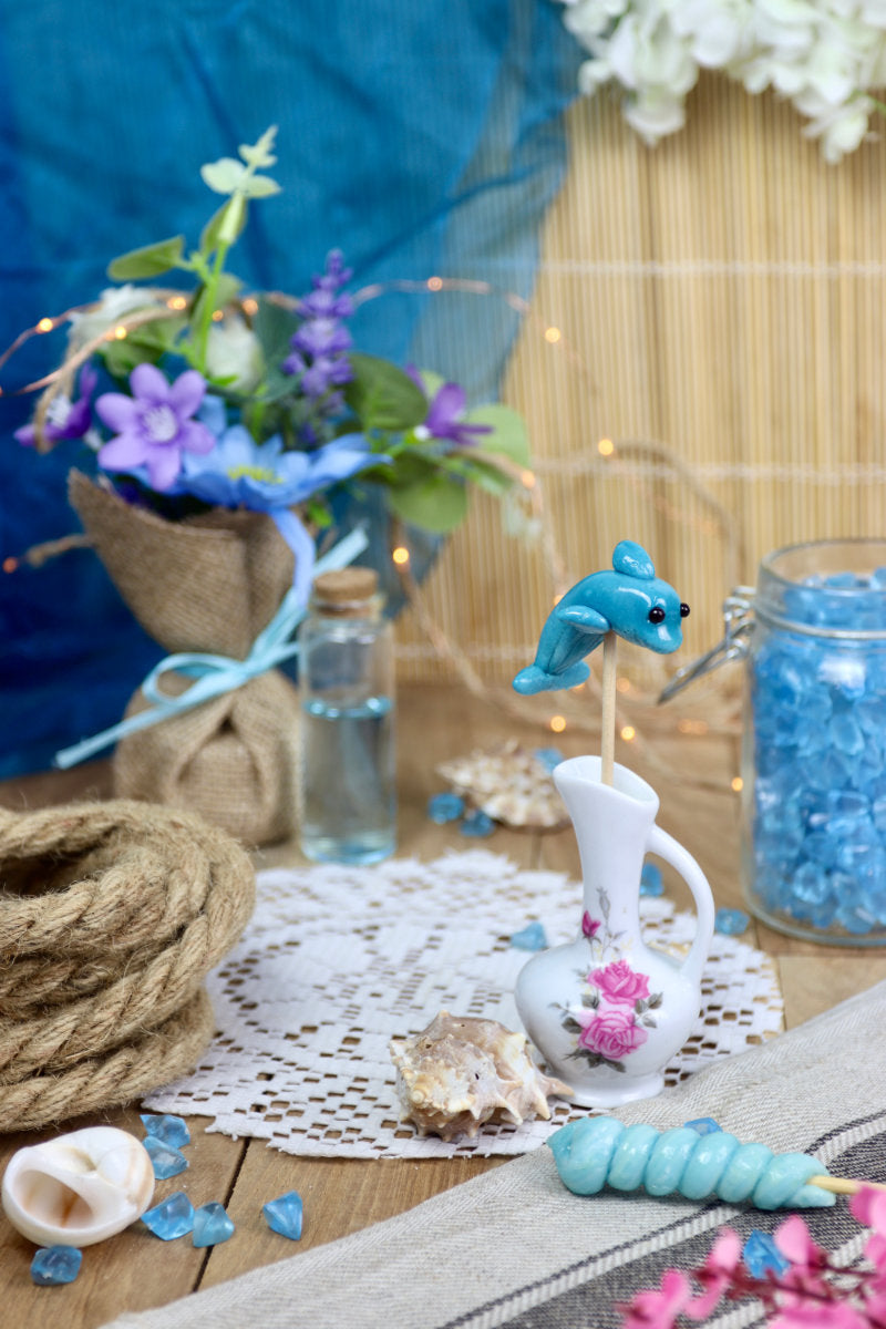 Sucette dauphin à la myrtille dans un décor marin, entourée de coquillages et d’éléments océaniques, parfaite pour un thème océan ou une décoration gourmande.