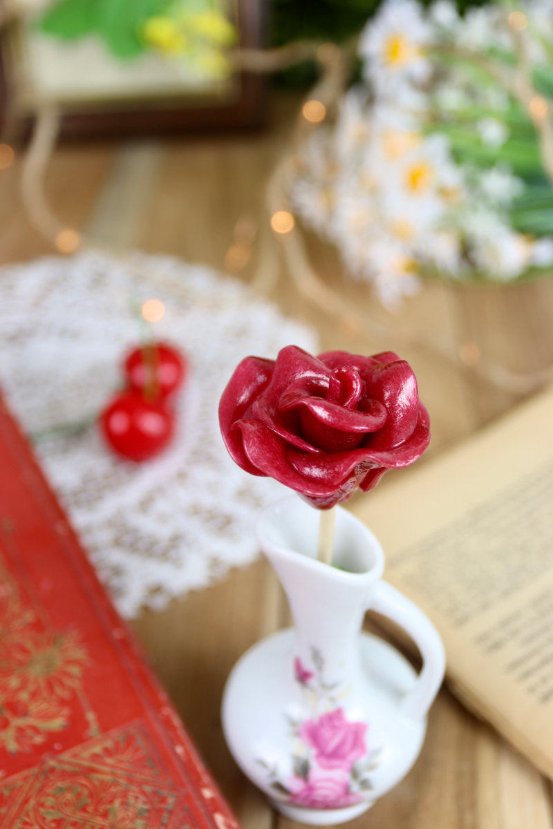 Sucette fleur cerise, présentée dans une ambiance romantique et fruitée, parmi des fleurs et des objets de fête.