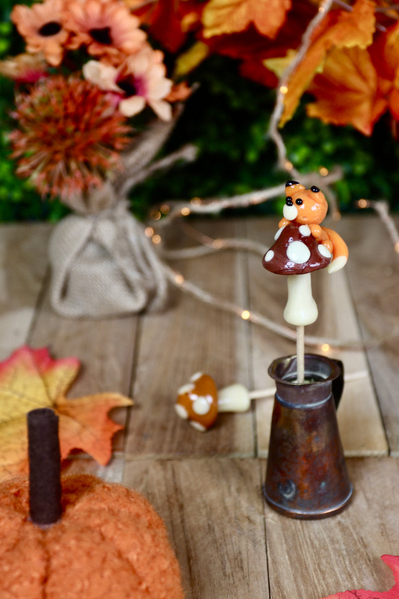 Sucette champignon avec renard, mise en scène dans un décor féerique d’automne avec mousse, feuilles et pommes de pin.