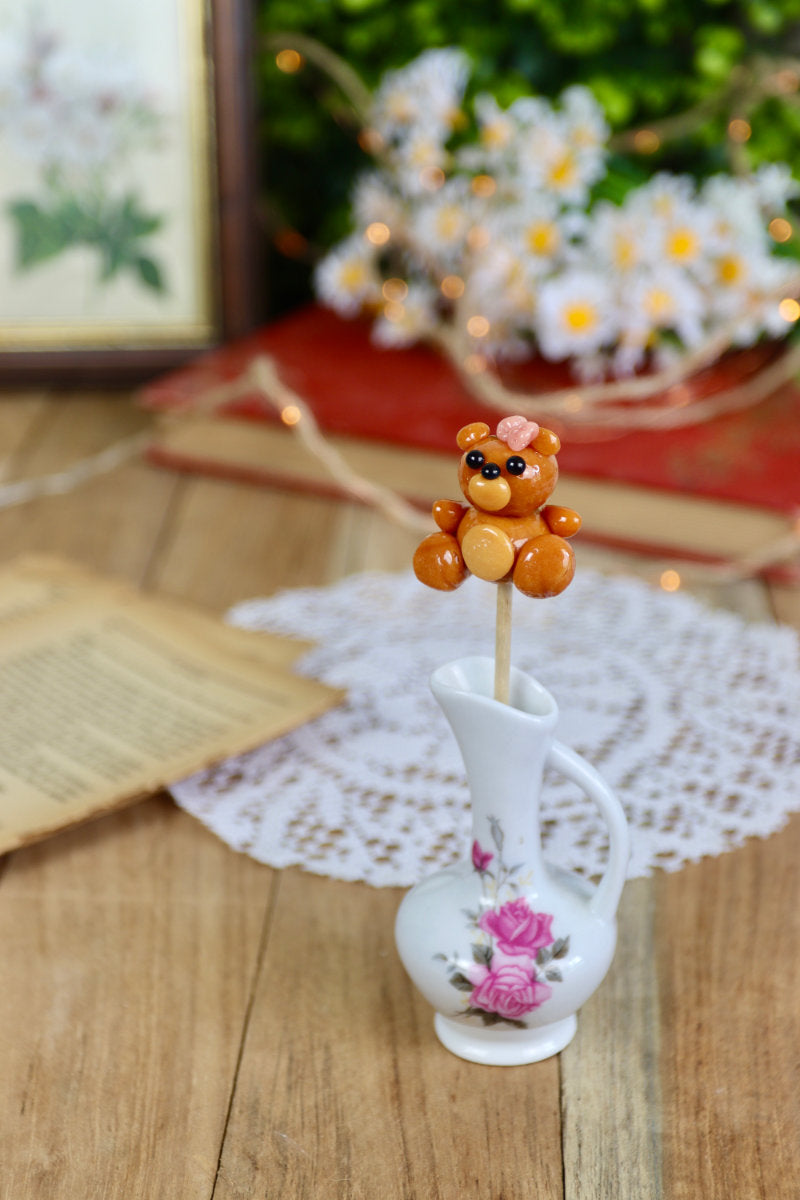 Sucette peluche caramel et framboise posée dans un décor enfantin et doux, parfait pour un cadeau ou une table de fête.