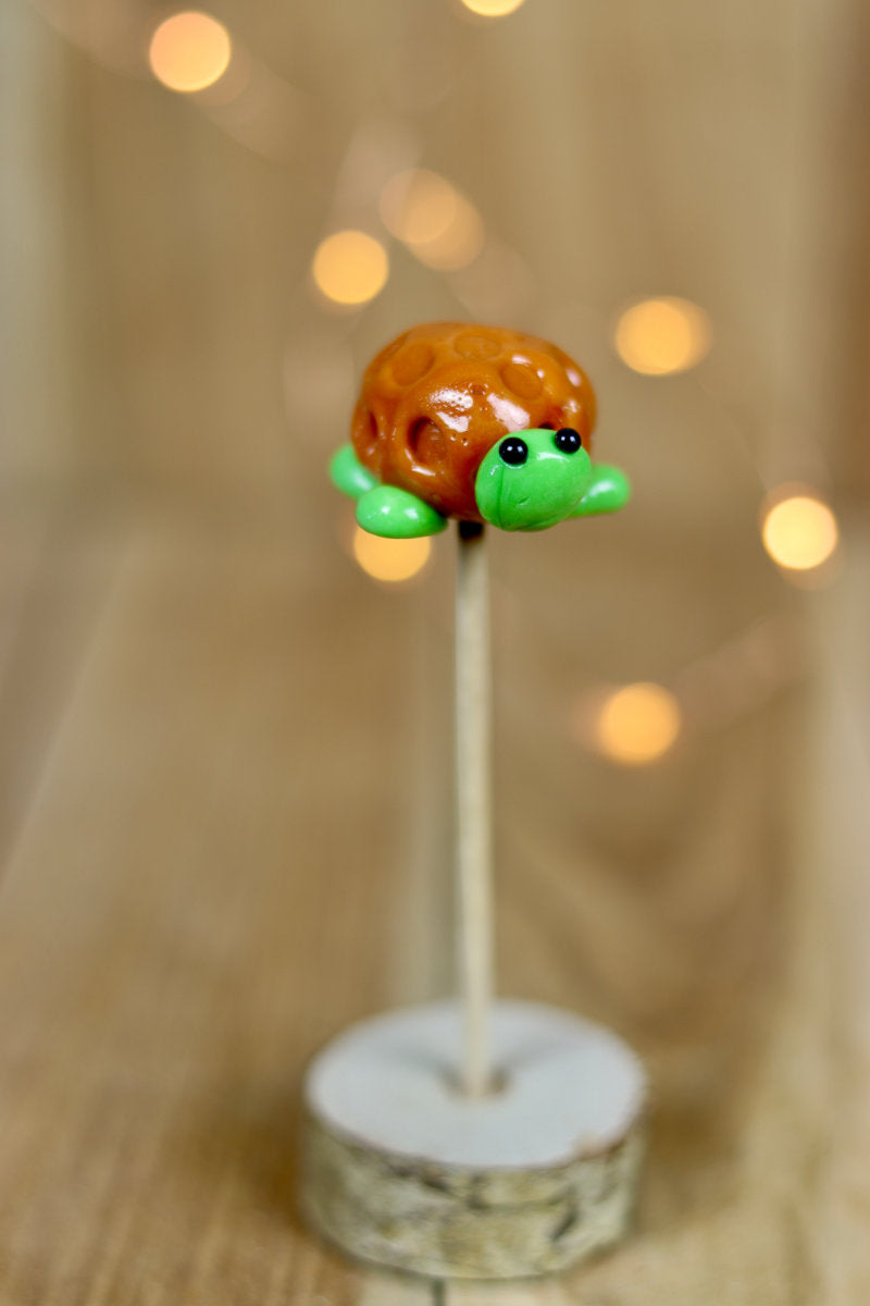 Une sucette sculptée à la main en forme de tortue. Elle est réalisée en sucre cuit aromatisé à la pomme et la carapace est au caramel.