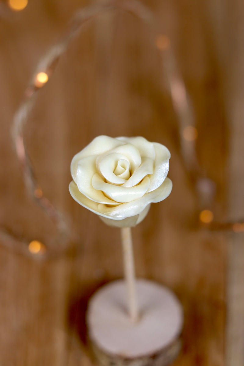Sucette sculptée en forme de fleur à la vanille. Elle est blanche et représente une rose