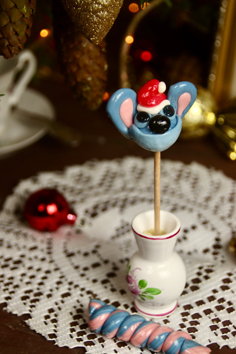 Sucette en forme de stitch avec un bonnet de noel myrtille fraise dans un déco féérique