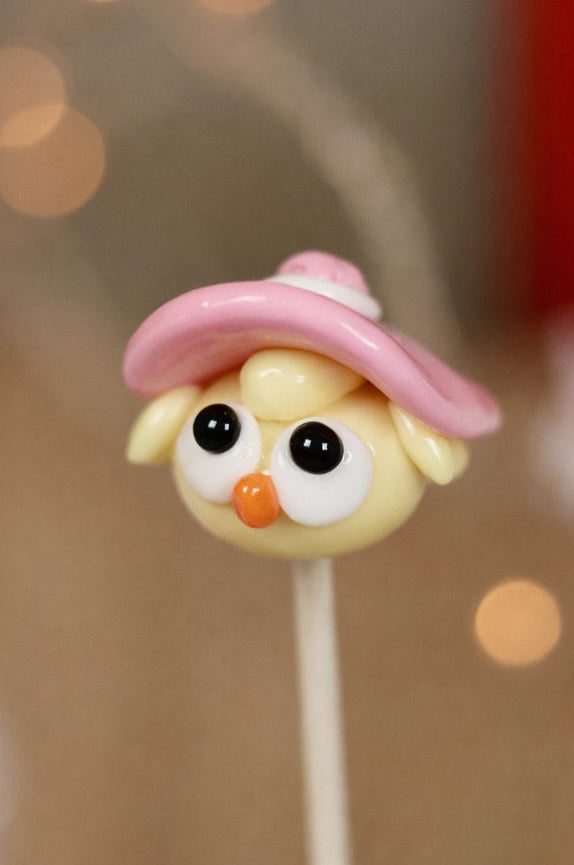 Sucette sculptée en forme de poussin à la pêche avec un chapeau sculptée à la fraise. Photo en gros plan sur la sucette avec une ambiance féérique
