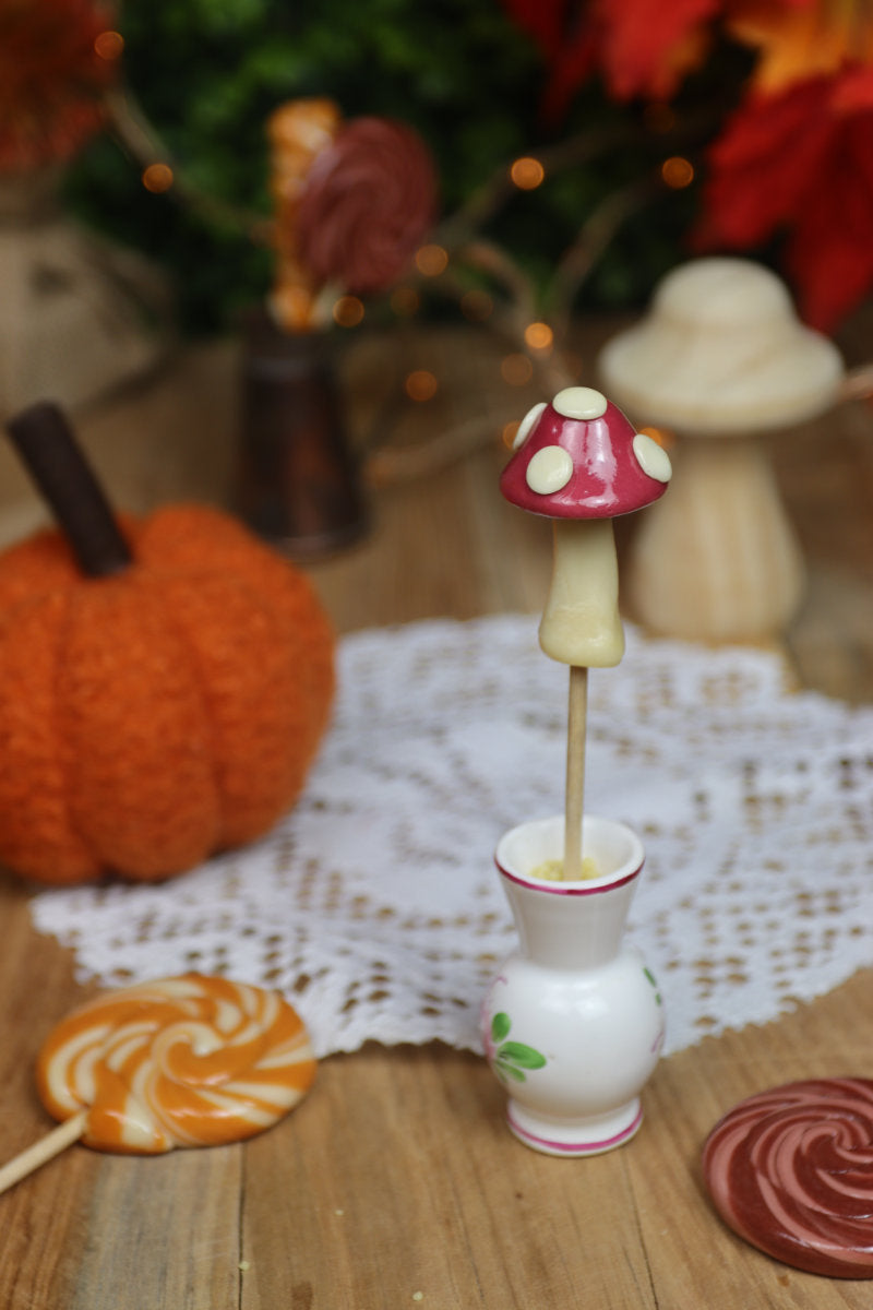 Sucette champignon vanille cassis posée dans un décor forestier aux couleurs douces