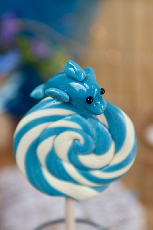 Sucette foraine en spirale bleu et blanche, sculptée à la main, décorée d’un dauphin, au goût myrtille et citron.