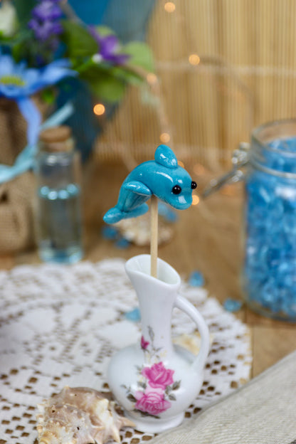 Sucette dauphin à la myrtille dans un décor marin, entourée de coquillages et d’éléments océaniques, parfaite pour un thème océan ou une décoration gourmande.