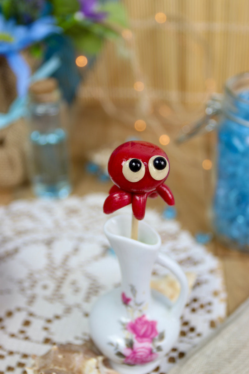 Sucette pieuvre à la cerise dans un décor marin, entourée de coquillages et d’éléments océaniques, idéale pour une ambiance féérique et gourmande.