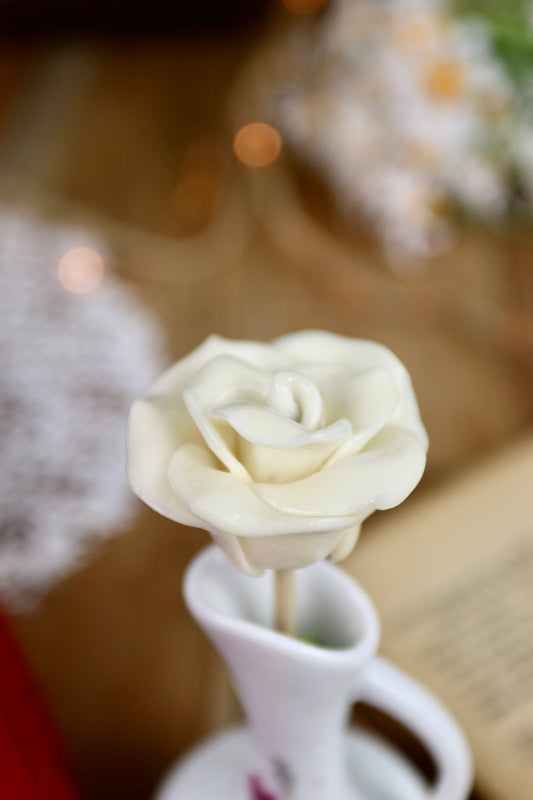Gros plan sur une sucette artisanale en forme de rose, sculptée à la main avec un parfum de noix de coco. Les pétales détaillés évoquent la douceur et l’élégance d’une fleur fraîche.