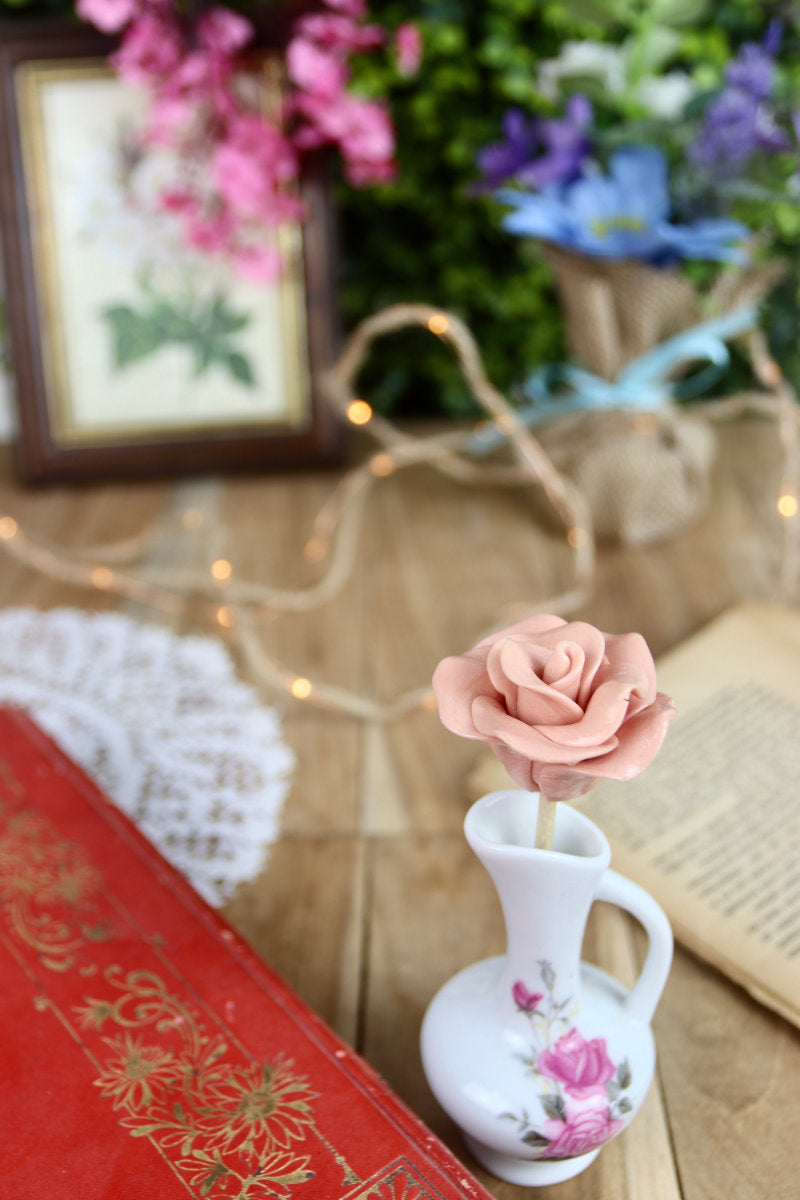 Sucette fleur à la framboise, présentée dans un décor naturel et romantique, parmi des fleurs champêtres et des objets décoratifs.