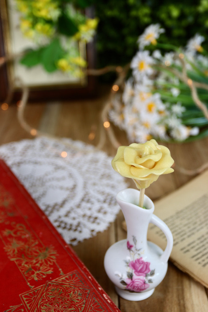 Sucette fleur à la pêche, présentée dans un décor printanier, parmi des fleurs naturelles et des objets de fête.
