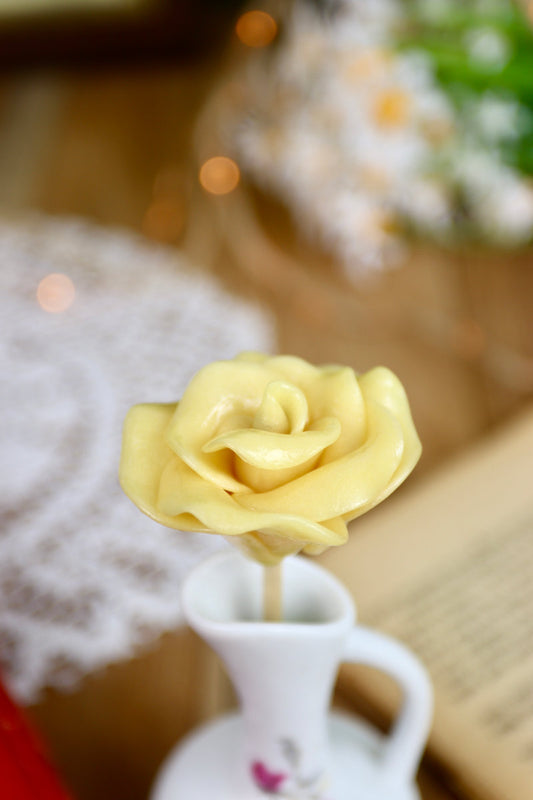 Gros plan sur une sucette artisanale en forme de rose, sculptée à la main avec un parfum de pêche. Les pétales détaillés rappellent une véritable fleur.