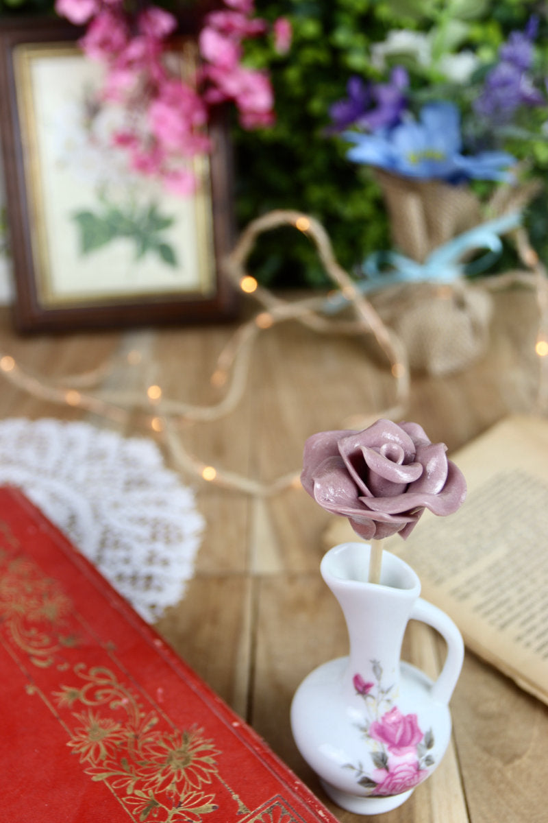 Sucette fleur à la violette, disposée dans un décor naturel et romantique, parmi des fleurs fraîches et des objets de fête.