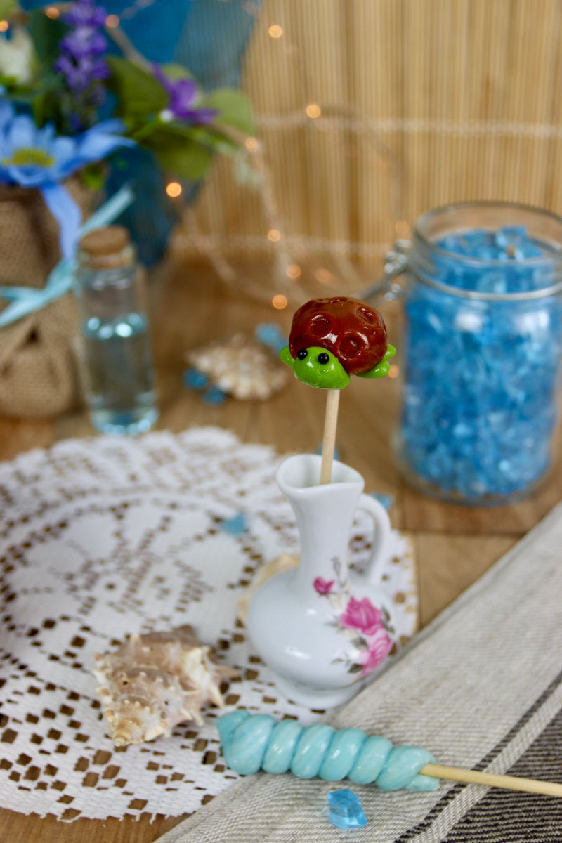 Sucette tortue pomme caramel dans un décor marin, entourée de coquillages et d’éléments océaniques, parfaite pour une décoration de table originale.