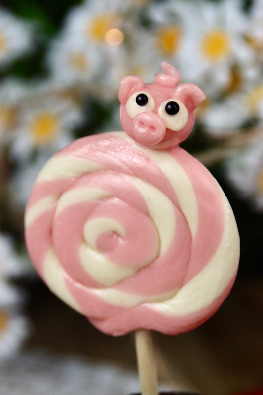 Gros plan sur une sucette foraine à spirale vanille-fraise avec un petit cochon rose sculpté à la main.