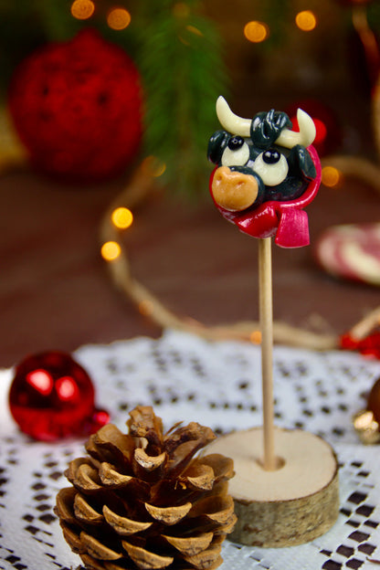 Une sucette en forme de taureau avec une écharpe à la cerise dans un décor féérique