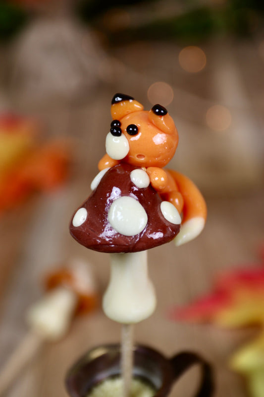 Sucette artisanale en forme de champignon vanille et cacao avec un petit renard orange grimpant dessus – saveurs vanille, cacao et orange.