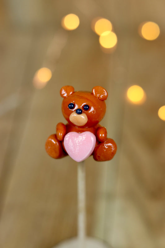 Sucette artisanale en forme de peluche au caramel avec un cœur rouge framboise sculpté sur le ventre.