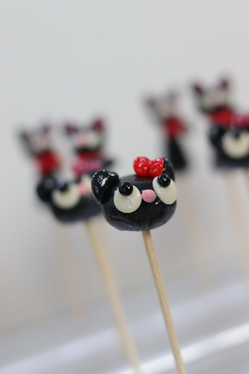 Production dans notre atelier français de sucette sculptée en forme de tête de chat noir ans un style kawaii, au cassis, avec des arôme naturels