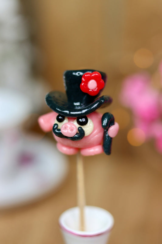 sucette sculptée en forme de cochon à la fraise habillé d'un chapeau au cassis. 