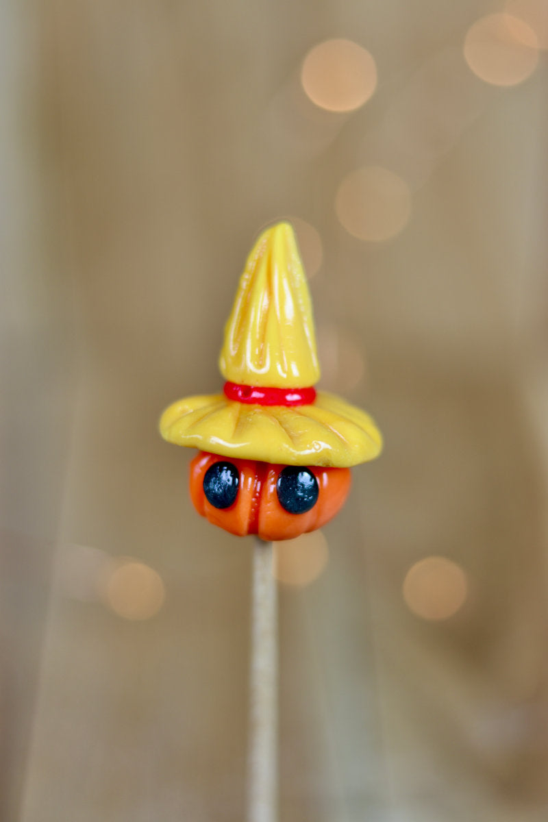 Sucette sculptée en forme d'épouvantail. Une citrouille avec des yeux coiffé d'un chapeau de paille à la pêche et à la cerise