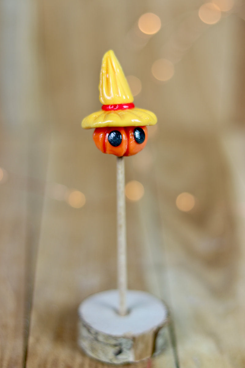 Sucette sculptée en forme d'épouvantail. Une citrouille avec des yeux coiffé d'un chapeau de paille à la pêche et à la cerise