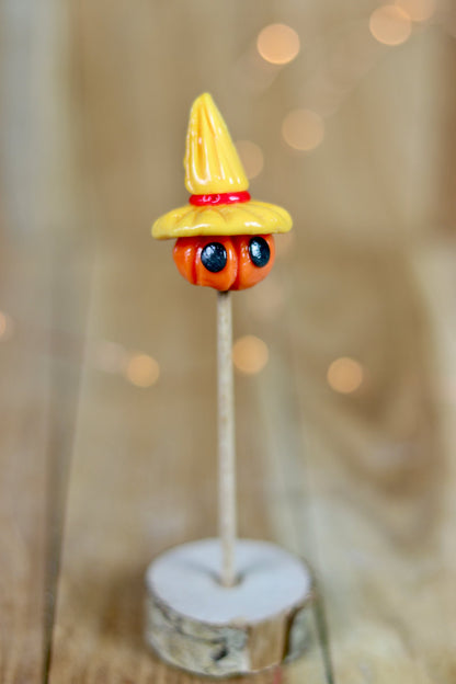 Sucette sculptée en forme d'épouvantail. Une citrouille avec des yeux coiffé d'un chapeau de paille à la pêche et à la cerise