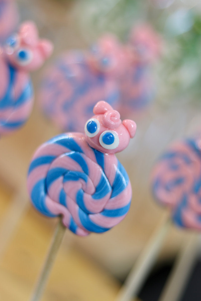 Une sucette foraine artisanale fraise myrtille avec un roudoudou sculptée dessus à la fraise dans l'atelier de fabrication