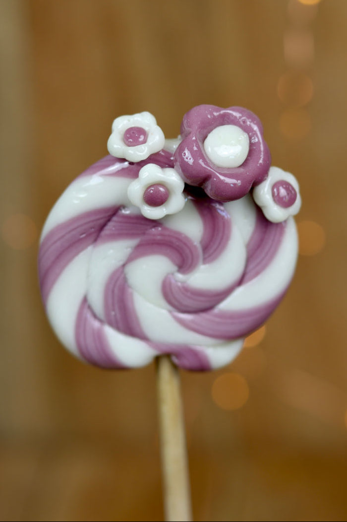 Sucette traditionnelle de forain avec des fleurs dessus à la violette et au citron