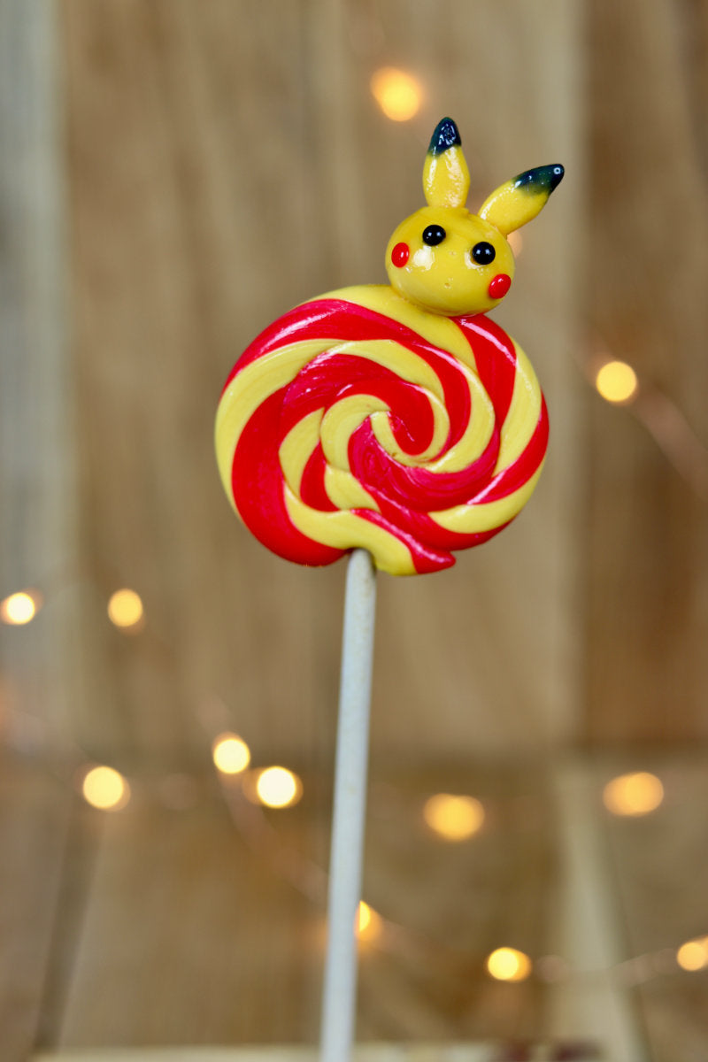 Sucette foraine banane cerise avec un pikachu sculptée à la banane dessus dans un décor féérique