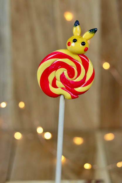 Sucette foraine banane cerise avec un pikachu sculptée à la banane dessus dans un décor féérique