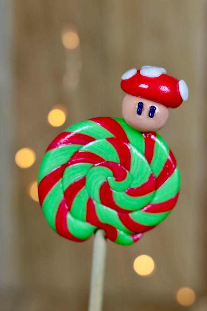 Une sucette foraine pomme cerise avec un champignon sculptée dessus. La sucette est dans un esprit Nintendo