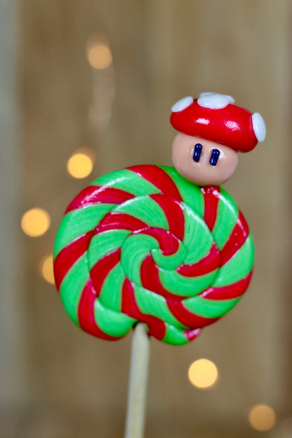 Une sucette foraine pomme cerise avec un champignon sculptée dessus. La sucette est dans un esprit Nintendo