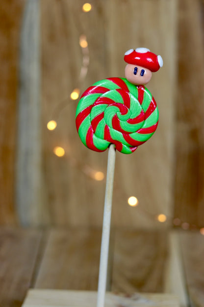 Une sucette foraine pomme cerise avec un champignon sculptée dessus. La sucette est dans un esprit Nintendo