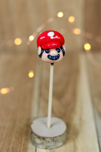 Sucette sculptée en forme de Mario à la banane et à la cerise dans un déco féérique