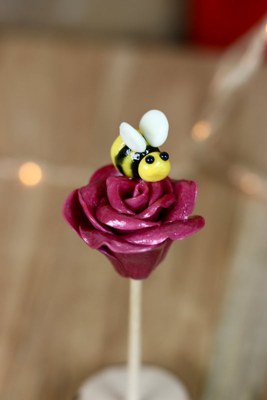 Sucette sculptée en forme de rose au cassis avec une abeille citron cassis qui butine