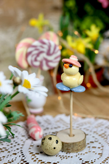 Une sucette sculptée en forme de canard à la pêche sur l'eau à la myrtille avec un chapeau sur la tête à la framboise. Dans un déco féérique et printanier