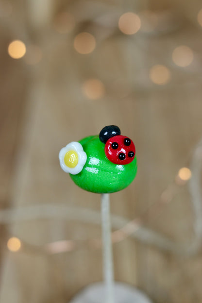 Sucette sculptée à la main en forme de boule verte à la pomme avec une fleur dessus et une coccinelle à la framboise dessus