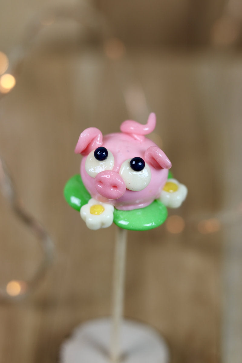 Une sucette sculptée en forme de cochon à la fraise dans une prarie de pâquerette