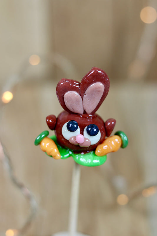 Sucette sculptée en forme de lapin au cacao au milieu d'un potager à la pomme avec des carottes à l'orange. 