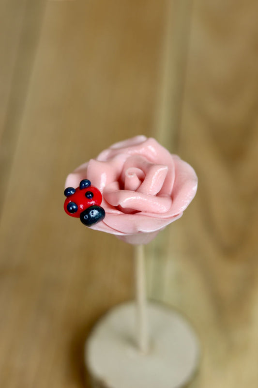 Une sucette sculptée en forme de rose à la framboise. Avec une coccinelle à la framboise dessus. En sucre cuit