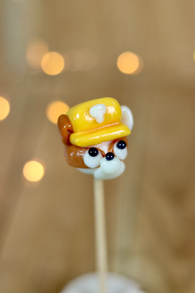 Une sucette sculptée à la main en forme de chien qui à un casque de chantier sur la tête, il est à la banane et au spéculoos. Il est inspiré de Ruben dans la PatPatrouille. 