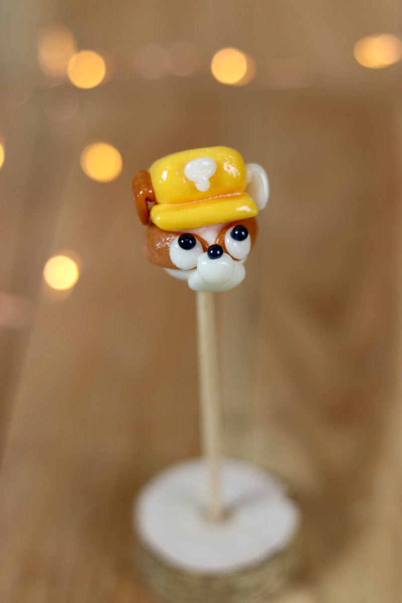 Une sucette sculptée à la main en forme de chien qui à un casque de chantier sur la tête, il est à la banane et au spéculoos. Il est inspiré de Ruben dans la PatPatrouille. 