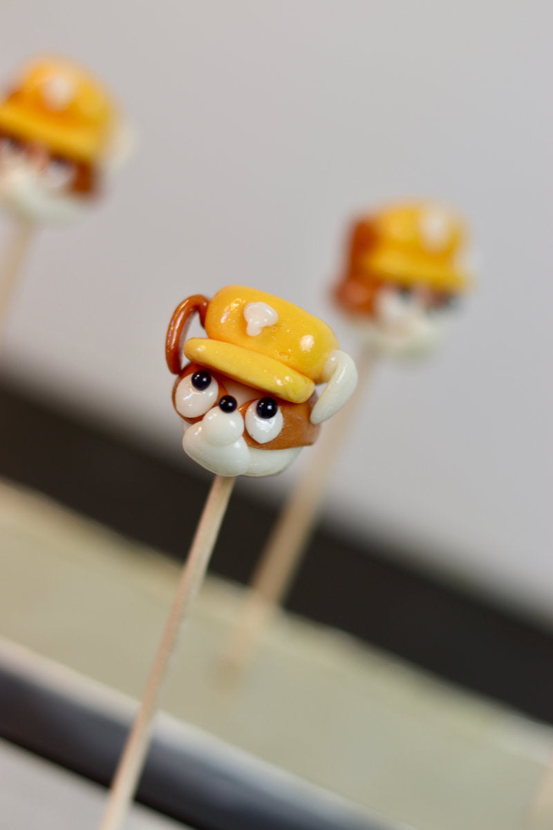 Une sucette sculptée à la main en forme de chien qui à un casque de chantier sur la tête, il est à la banane et au spéculoos. Il est inspiré de Ruben dans la PatPatrouille. Photo prise dans notre atelier de fabrication en Bourgogne