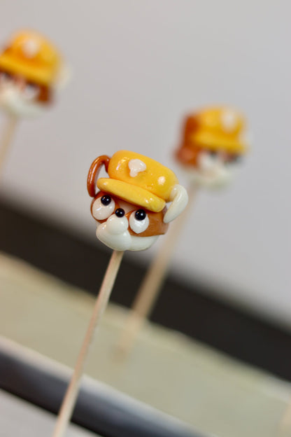 Une sucette sculptée à la main en forme de chien qui à un casque de chantier sur la tête, il est à la banane et au spéculoos. Il est inspiré de Ruben dans la PatPatrouille. Photo prise dans notre atelier de fabrication en Bourgogne
